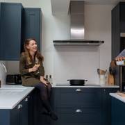 Amy sitting on the kitchen counter with a wine glass in hand while Kamal stands by the kitchen island pouring a glass of wine for himself.