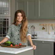 Siri Barje står vid köksön i sitt nya lantliga kök Fagerö i gröna kulören Tall från Marbodal, med bänkskiva Bianco Carrara som köksbänk och stänkskydd.