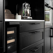 Et nydelig svart kjøkken i lun eik med kjøkkenøy dekket av lys komposittstein og stilige matt-svarte håndtak.