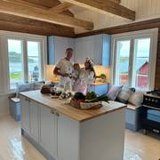 Keittiössä keittiösaareke, karmiovet erikoissävyssä NCS S 1020-R90B 1800-luvun hirsitalossa, tammitasot, posliinitiskiallas ja messinkihana.