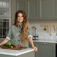 Siri Barje står vid köksön i sitt nya lantliga kök Fagerö i gröna kulören Tall från Marbodal, med bänkskiva Bianco Carrara som köksbänk och stänkskydd.