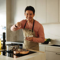 Filip Poon lagar mat i sitt clean och eleganta Arkitekt Plus Sand-kök från Marbodal med Dekton-bänkskiva och matchande stänkskydd