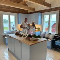 Keittiössä keittiösaareke, karmiovet erikoissävyssä NCS S 1020-R90B 1800-luvun hirsitalossa, tammitasot, posliinitiskiallas ja messinkihana.