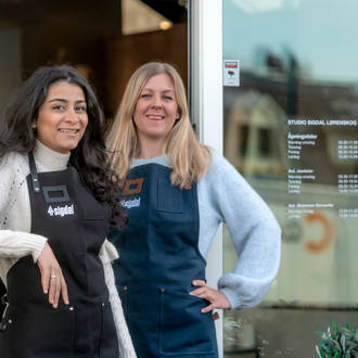 Kjøkkendesignere i skjorter og forklær smiler til kameraet utenfor Sigdals butikk