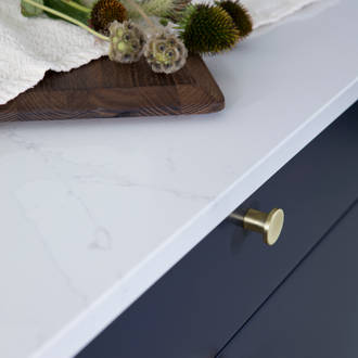 Lähikuva messinkinupeista tummansinisissä Meri keittiön laatikoissa, joissa on valkoinen marmoroitu työtaso