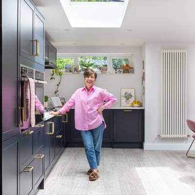Marina smiling in her bold and welcoming dark blue Dunham Midnight kitchen from Magnet, with tall cabinets and open shelves.