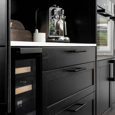 Et nydelig svart kjøkken i lun eik med kjøkkenøy dekket av lys komposittstein og stilige matt-svarte håndtak.