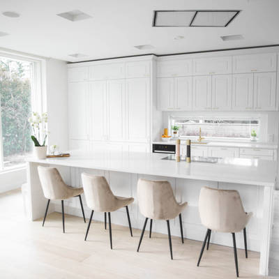 Valkoinen keittiö, jossa perinteiset maalatut karmiovet, messinkikahvat ja marmoroitu työtaso, keittiösaareke istuimilla.