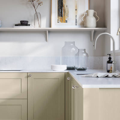 Ludlow, a traditional Shaker-style premium feel kitchen range with a visible woodgrain on its panelled doors here shown in the shade Parchment styled with steel knobs, steel tap, a white marbled worktop with matching splashback.