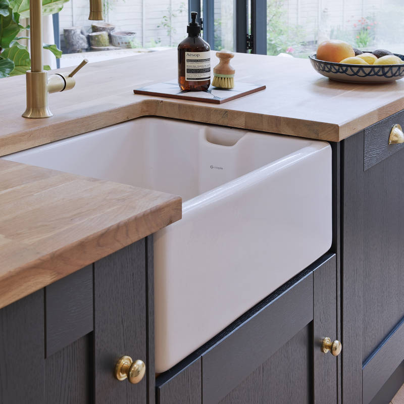 Close-up of Caple Belfast Ceramic sink which adds a rustic charm to the kitchen island. Paired with a wood worktop and brass tap.