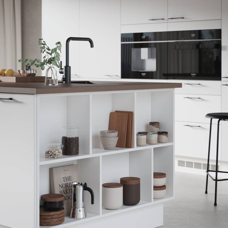 Hvit kjøkken og kjøkkenøy med slank og elegant front med svakt avrundede kanter, Corestoen varm sement benkeplate, sort kran, endehyller i kjøkkenøya.