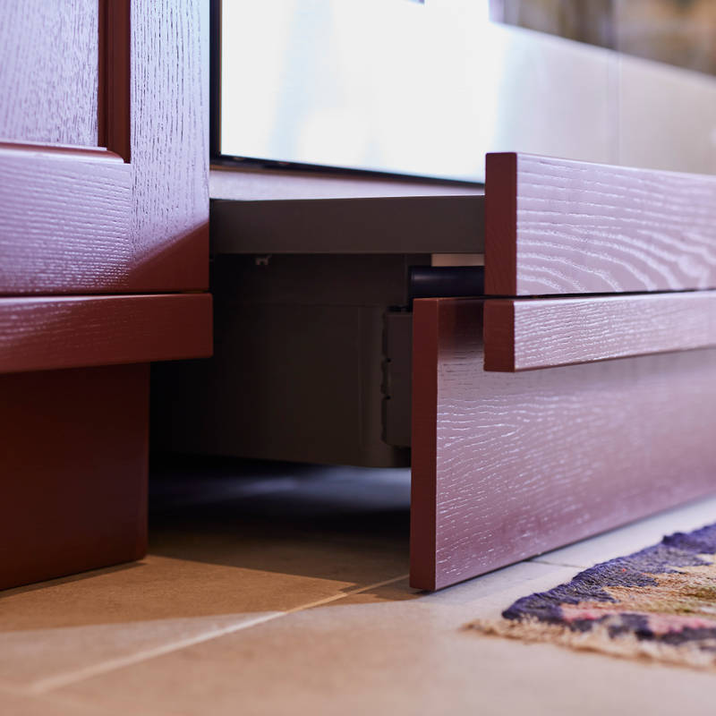 Close-up of pulled out drawers under oven in kitchen island, with traditional Shaker style fronts Ludlow Burlington red, with a tactile woodgrain.