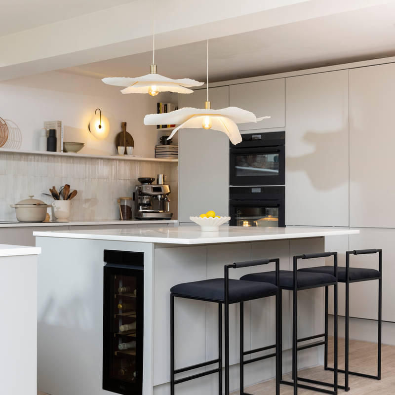 Diagnonal view of kitchen island corner in Yasmin Wyatt's open, light and airy neutral shade handleless Luna kitchen from Magnet with a white Corian worktop in Onyx, two AEG ovens integrated into tall cabinet and a wine cooler integrated into kitchen island.