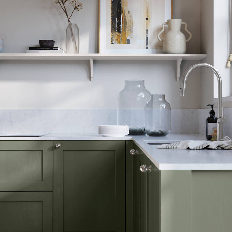 Wardley Thyme kitchen cabinetry with steel knobs, steel tap, white marbled worktop and matching backsplash. An open shelf on the wall above cabinets with ceramics and a vase of flowers.
