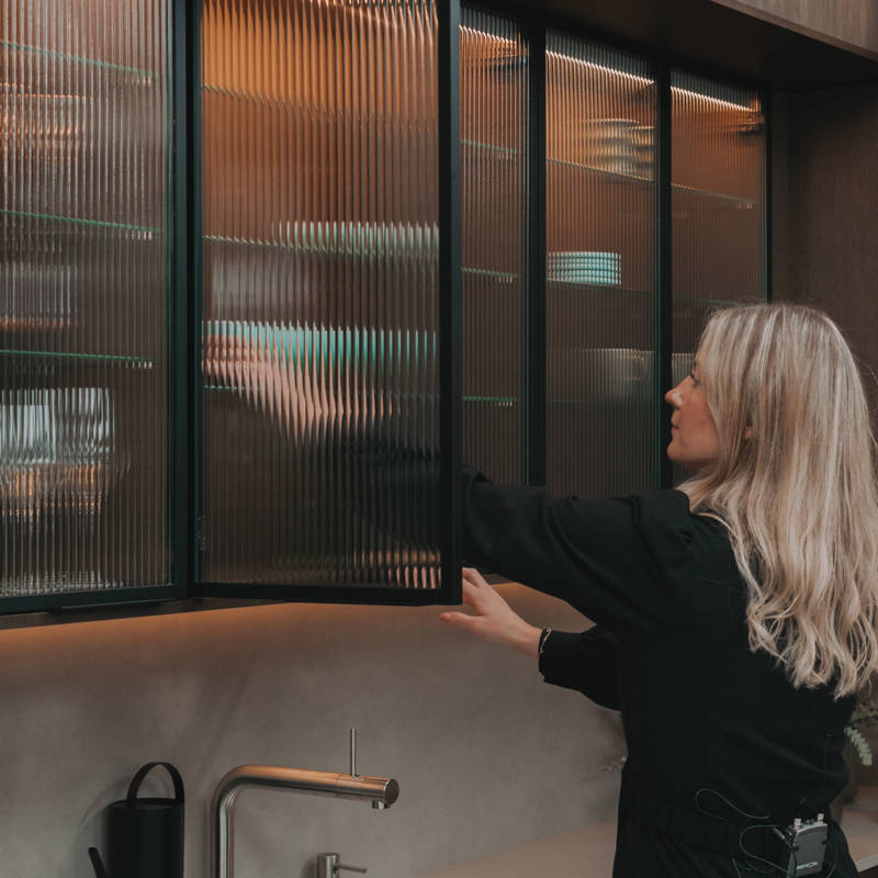 Hanna Stenseth i kjøkkenet Favn fra Sigdal i lekker eikefinér, som er beiset i fargen Nøtt, kjøkkenøya og vitrinedører med bølget glass og sorte aluminiumsrammer i God Morgen Norge studion sin