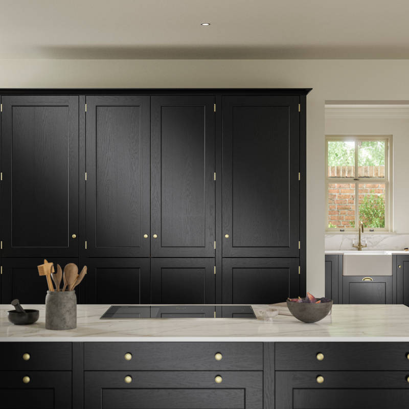 View over kitchen island in Traditional Shaker-style tactile woodgrain Ludlow Sumi Black kitchen with tall cabinets, brass accessories, marbled white and grey worktop, white ceramic sink and brass tap.