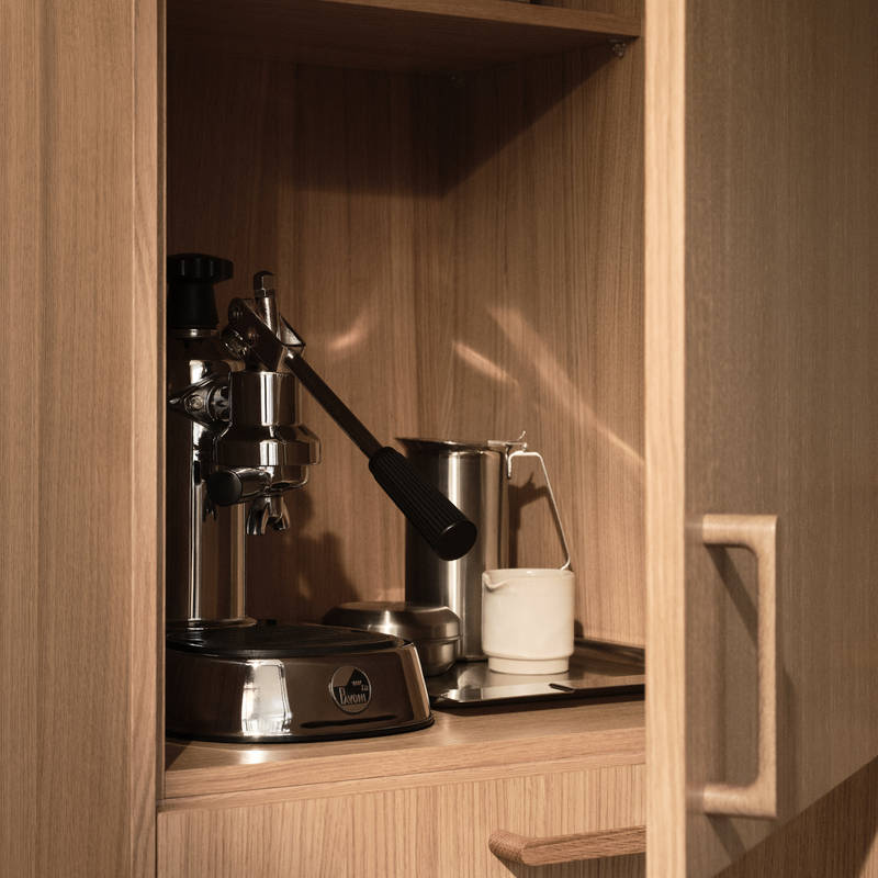 Öppnat skåp i Siri Barjes kök, ekskåp med kaffemaskin i skåpet, handtag i ek.