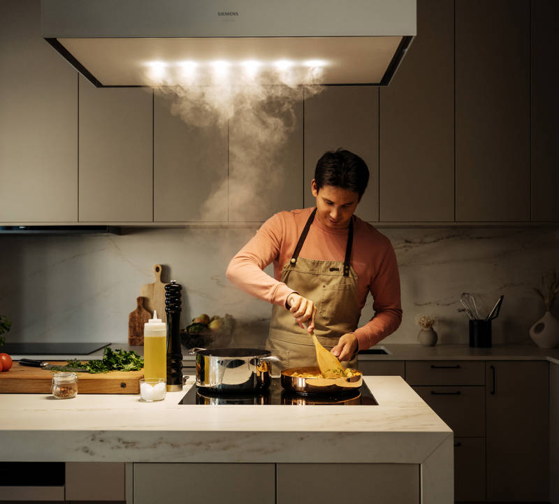 Filip Poon lagar mat i sitt clean och eleganta Arkitekt Plus Sand-kök från Marbodal med Dekton-bänkskiva och matchande stänkskydd