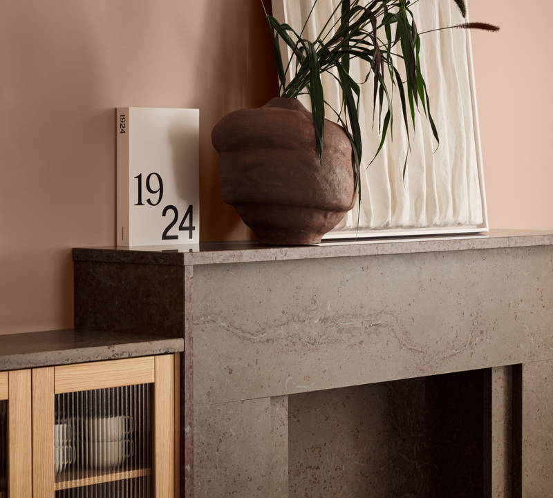 Öppen spis med växt i keramik-kruka intill vitrinskåp med träram i natur ek och räfflat glas