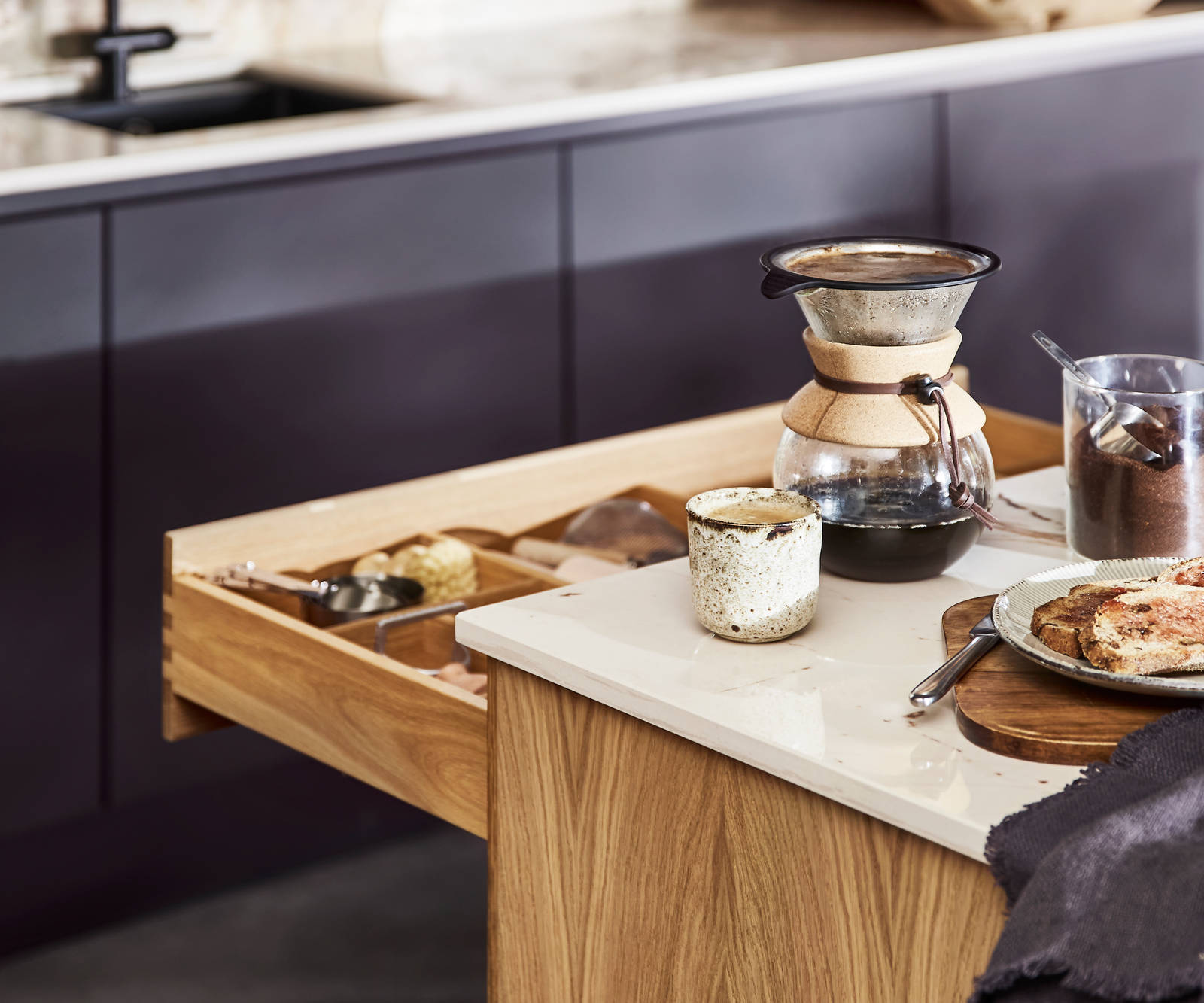 Close-up of opened oak drawer in Nordic Craft kitchen island, with breakfast served on handmade ceramics on the worktop.