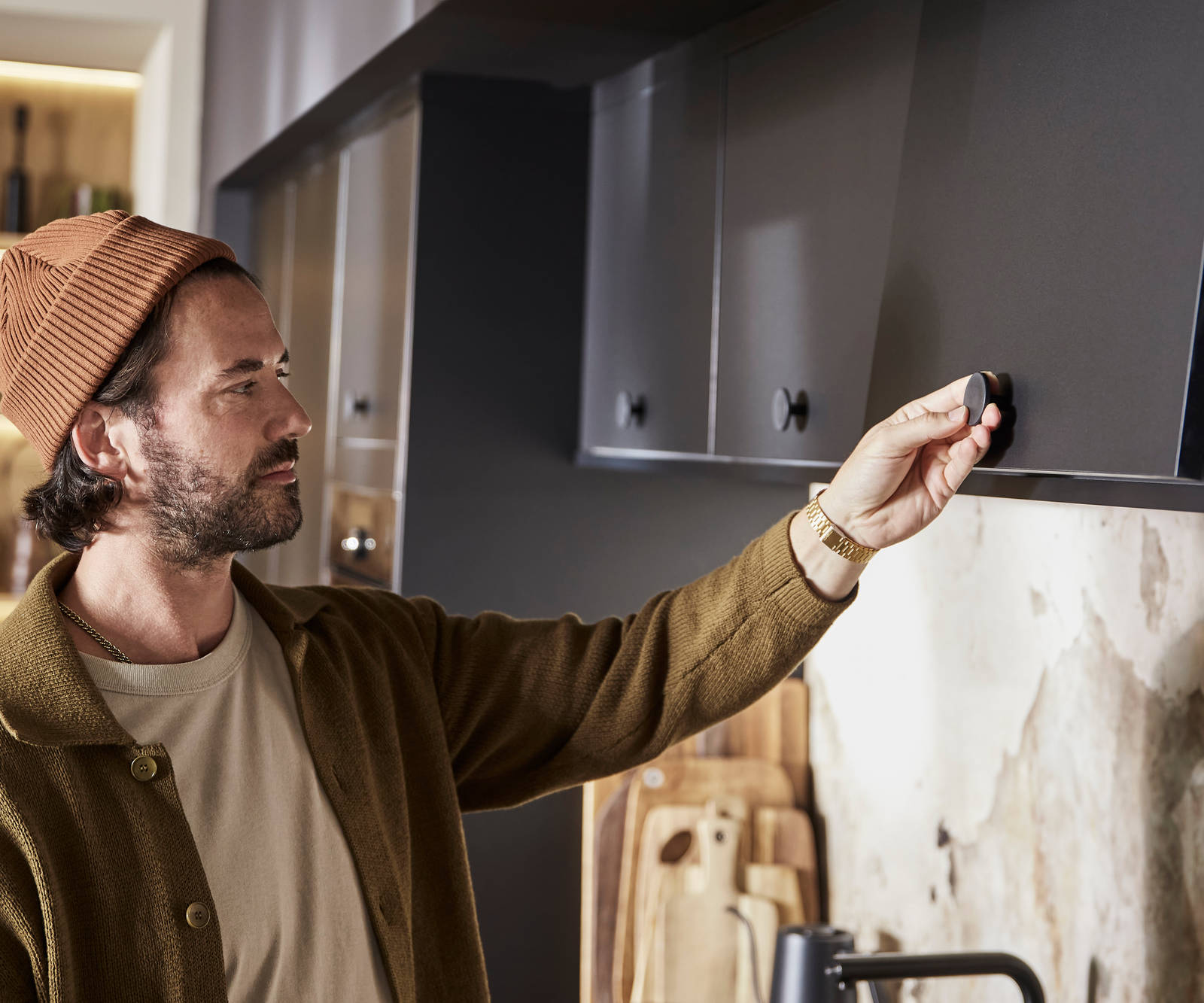 Man wearing clothes in earth tones opening a top cabinet in Hoxton Sumi Black