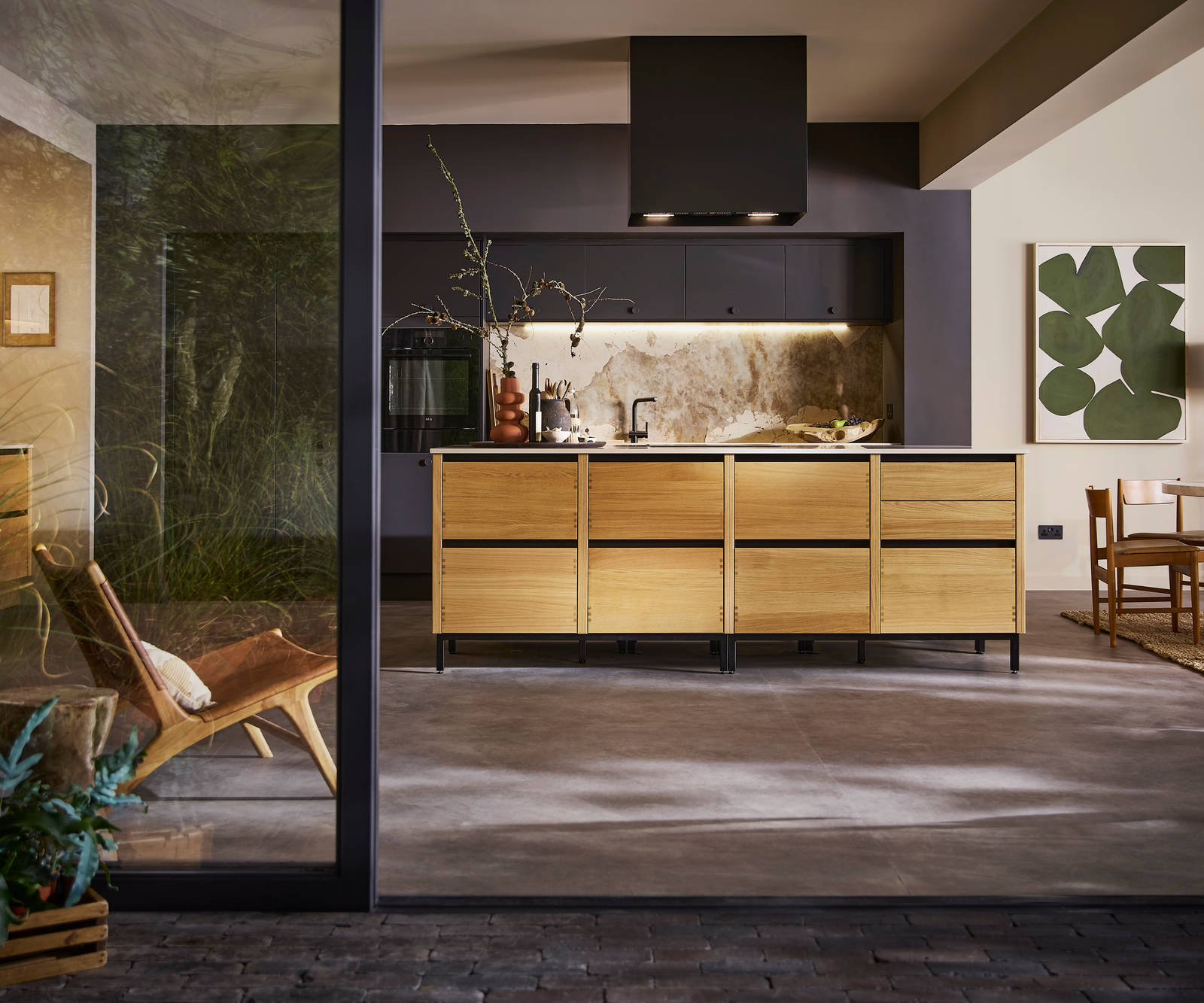 Open floorplan kitchen Mindful World, view from outside open glass foors to patio, with kitchen table and black ceiling-mounted Roroshetta Mantica Sense.