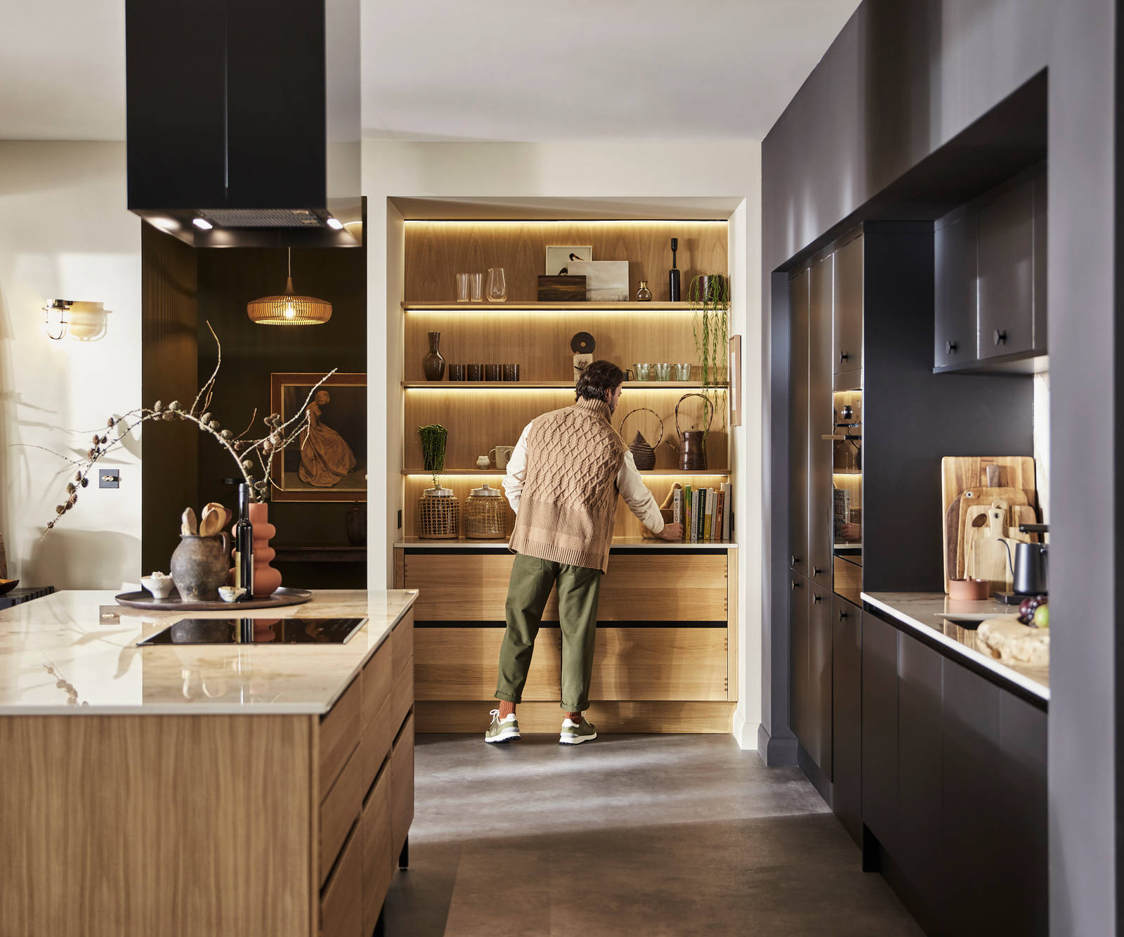 Man organising reaching for cook book in natural oak open shelves with matching wall paneling over Nordic Craft cabinetry.