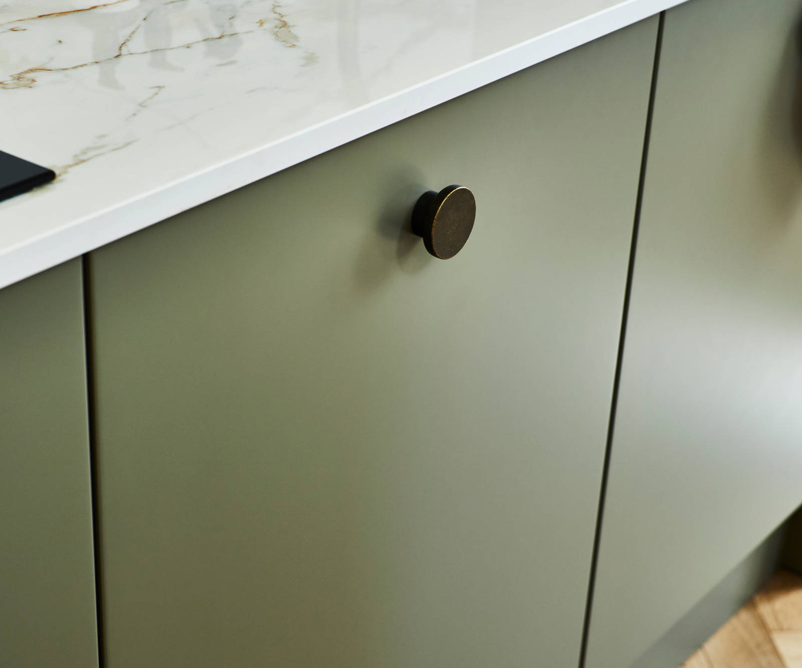Close-up of Soho green Balmoral cabinet and black handles, with light gray marble worktop and white sink.