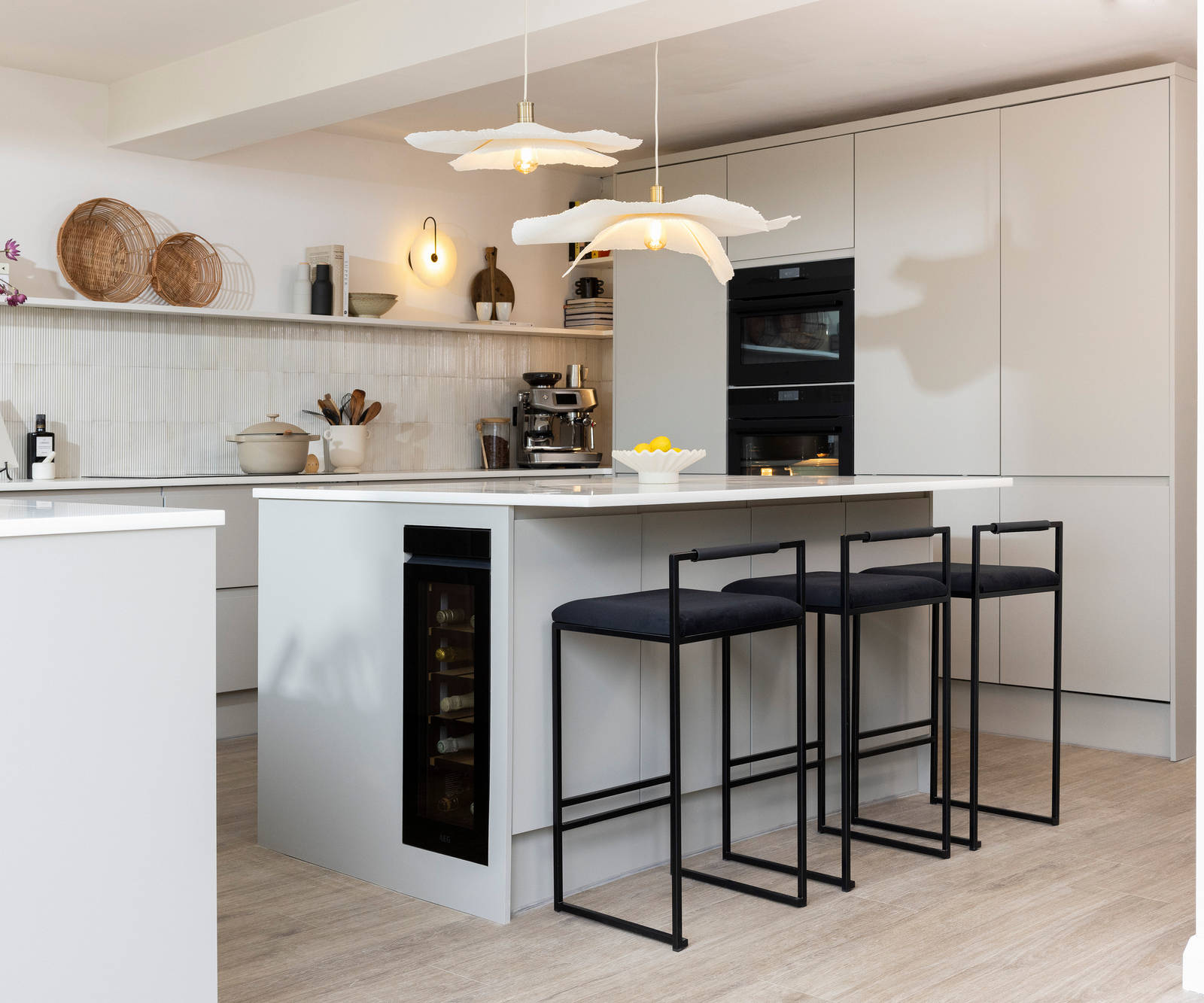 Diagnonal view of kitchen island corner in Yasmin Wyatt's open, light and airy neutral shade handleless Luna kitchen from Magnet with a white Corian worktop in Onyx, two AEG ovens integrated into tall cabinet and a wine cooler integrated into kitchen island.