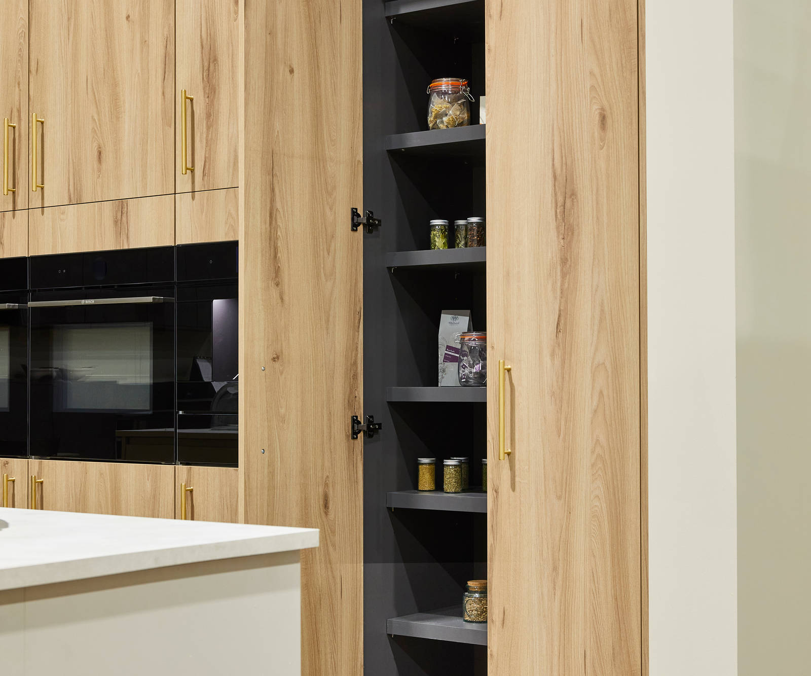 Magnet's modern Portobello kitchen in a light woodgrain décor, larders finished with brass bar handles.