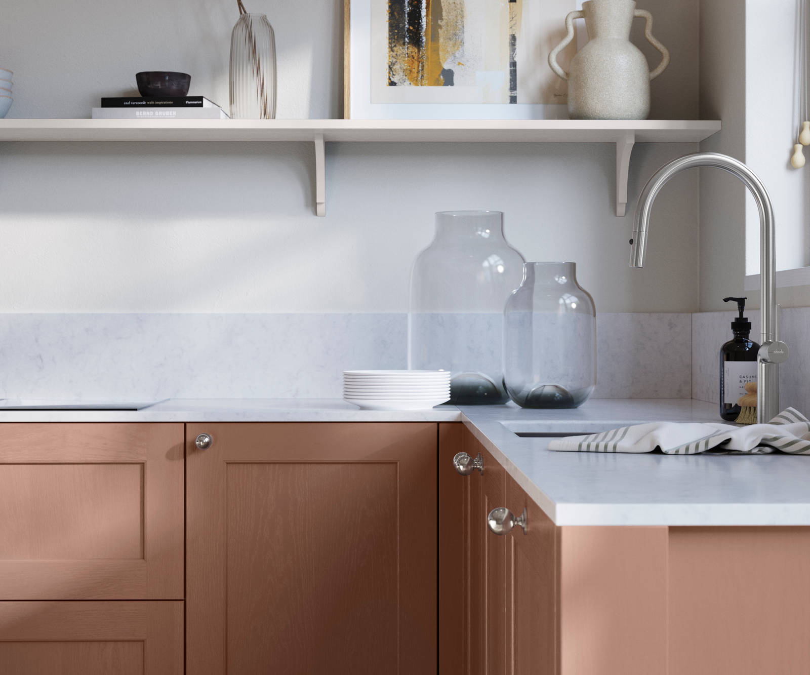 Ludlow, a traditional Shaker-style premium feel kitchen range with a visible woodgrain on its panelled doors here shown in the shade Clay styled with steel knobs, steel tap, a white marbled worktop with matching splashback.