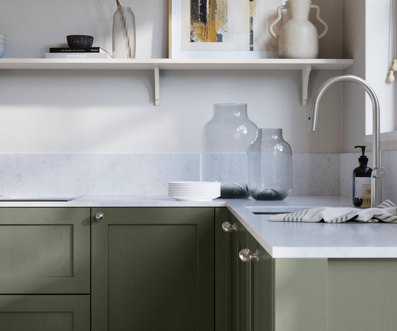 Wardley Thyme kitchen cabinetry with steel knobs, steel tap, white marbled worktop and matching backsplash. An open shelf on the wall above cabinets with ceramics and a vase of flowers.