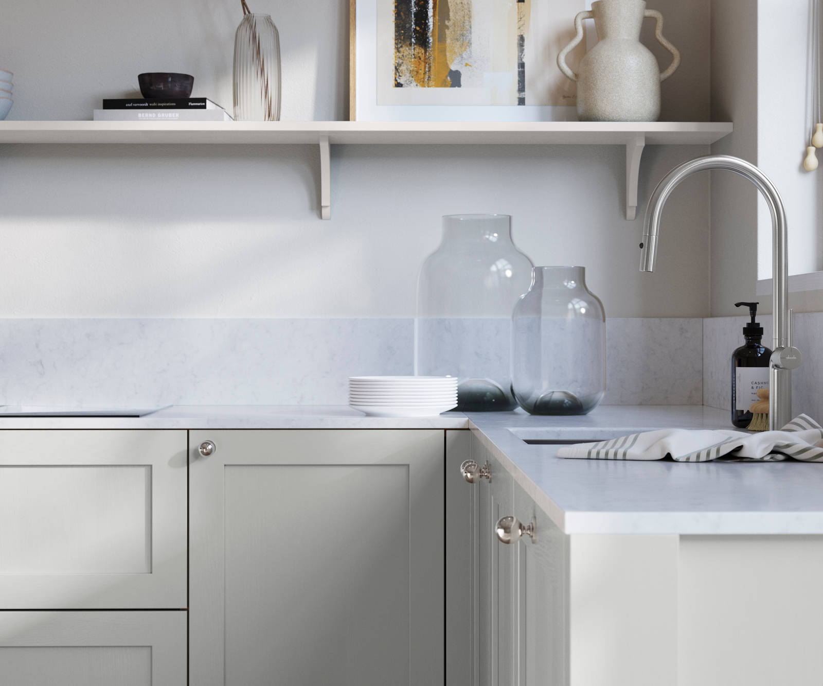Wardley Washed Cotton kitchen cabinetry with steel knobs, steel tap, white marbled worktop and matching backsplash. An open shelf on the wall above cabinets with ceramics and a vase of flowers.