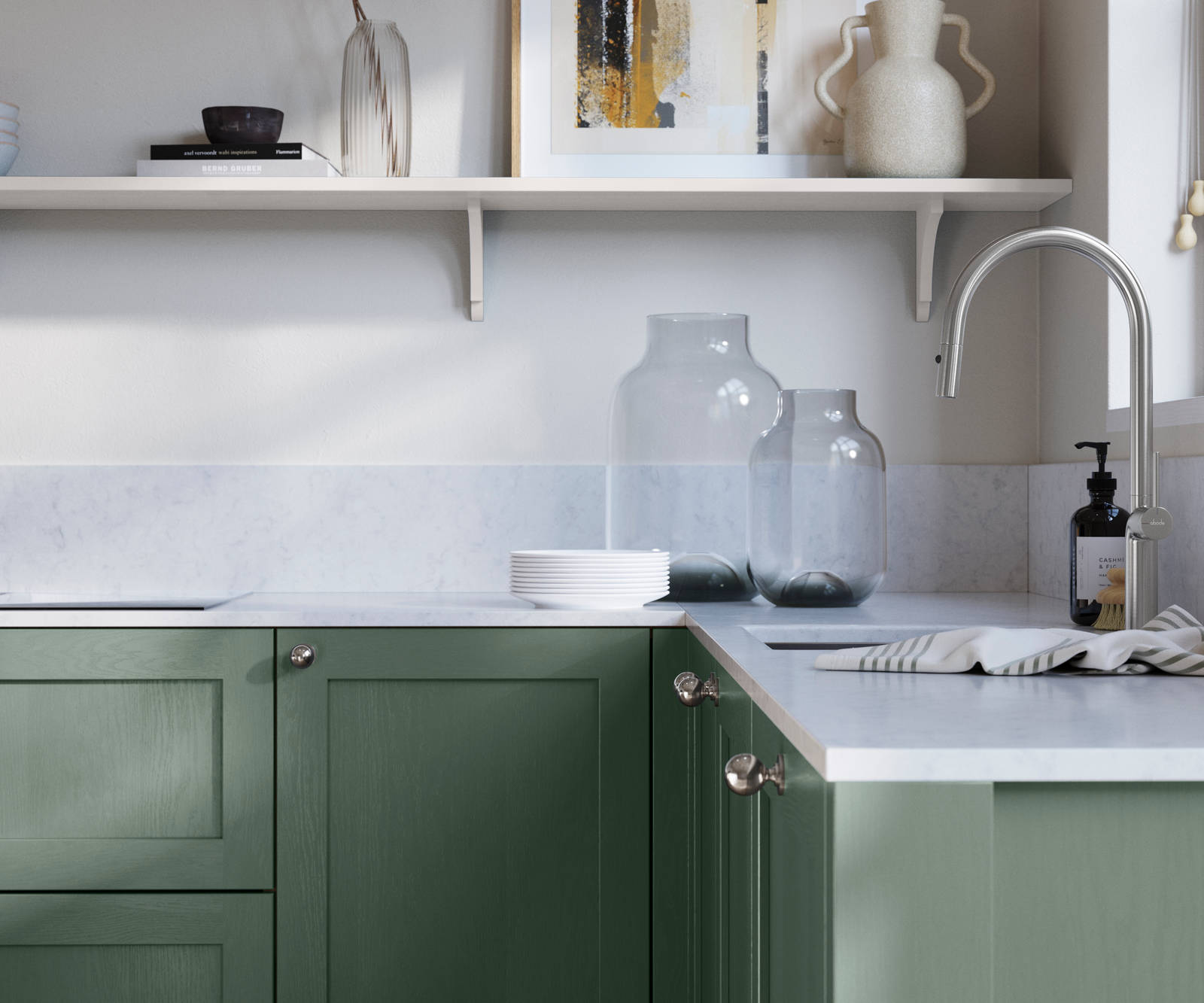 Wardley Eucalyptus kitchen cabinetry with steel knobs, steel tap, white marbled worktop and matching backsplash. An open shelf on the wall above cabinets with ceramics and a vase of flowers.
