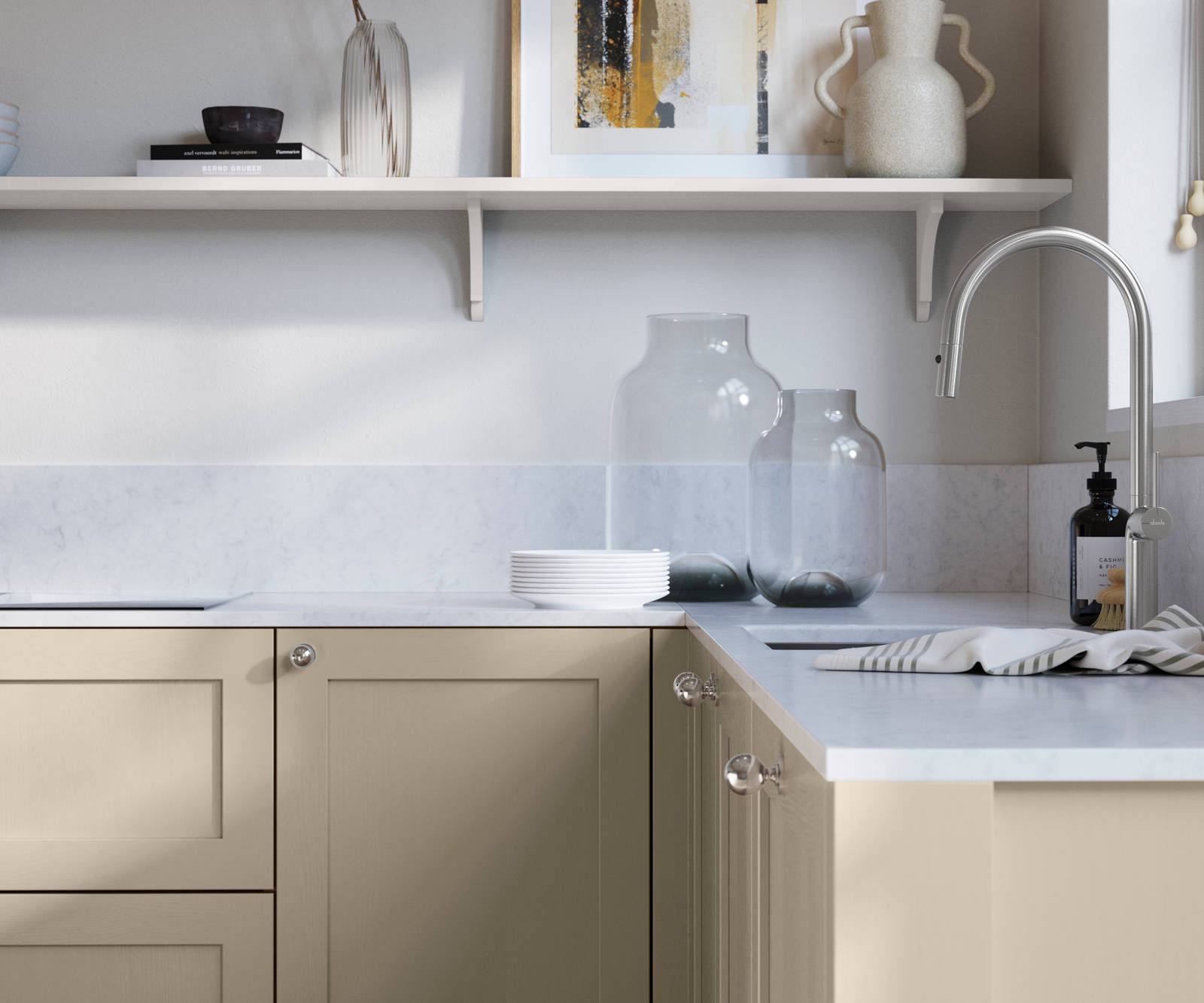 Wardley Pebble path kitchen cabinetry with steel knobs, steel tap, white marbled worktop and matching backsplash. An open shelf on the wall above cabinets with ceramics and a vase of flowers.
