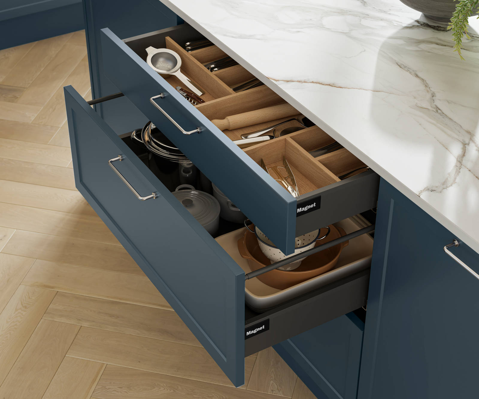Pulled out drawers in Brunswick Voyage blue kitchen island with oak cutlery inserts, white and grey marbled worktop and light wood herringbone flooring.