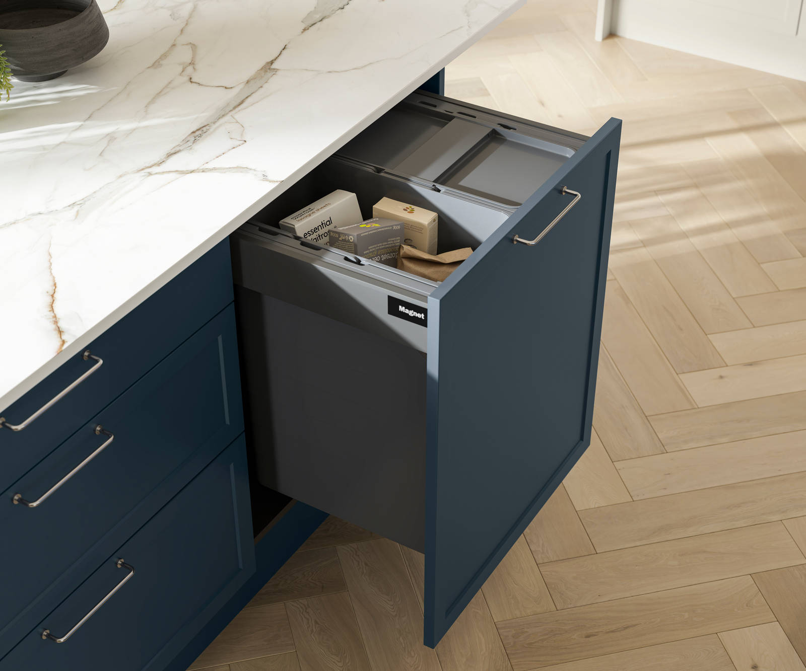Pulled out drawer in Brunswick Voyage blue kitchen island with interior for waste recycling, white and grey marbled worktop and light wood herringbone flooring.