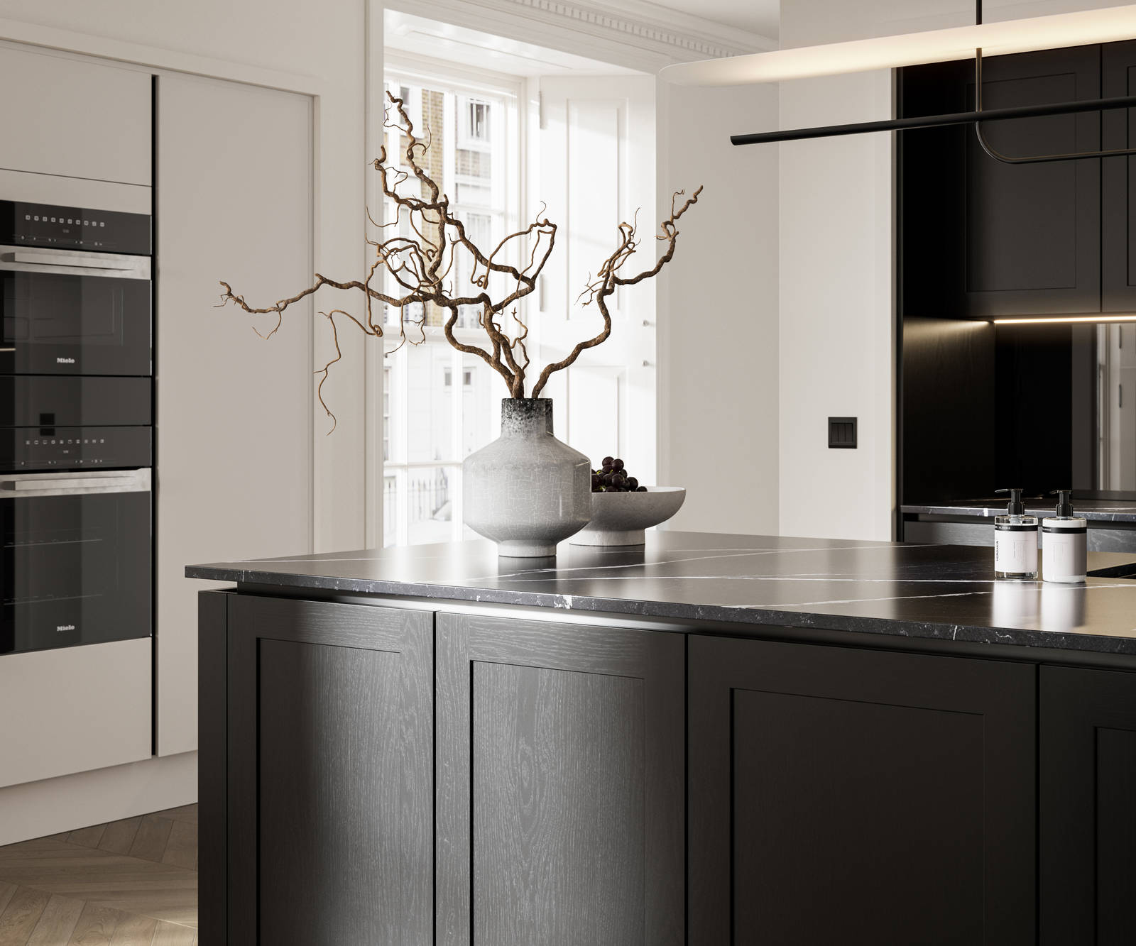 Handleless frame doors Integra Wardley Sumi black kitchen with kitchen island, Integra Soho Limestone tall cabinets with integrated ovens, natural shade ceramic vase holding foliage branches.