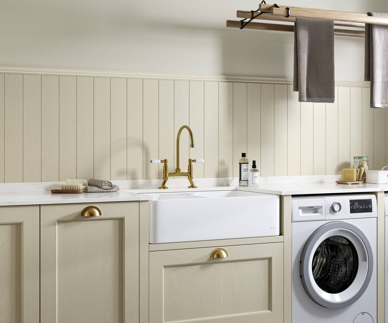 Traditional Shaker-style Ludlow Parchment and French Clay utility room with white ceramic sink, washing machine and tumble dryer with white marbled Silestone worktop and upstand, wallpanel matching the cabinetry, traditional brass tap and towels hanging on wood drying rack.
