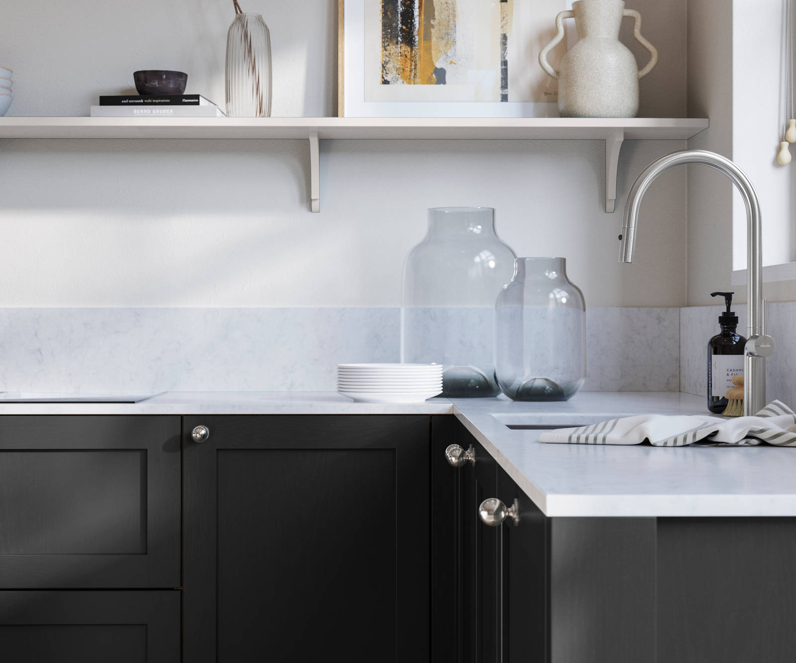 Wardley Sumi Black kitchen cabinetry with steel knobs, steel tap, white marbled worktop and matching backsplash. An open shelf on the wall above cabinets with ceramics and a vase of flowers.