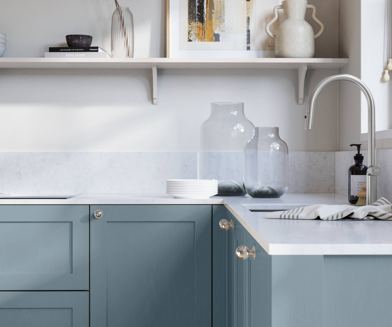 Wardley Portland Blue kitchen cabinetry with steel knobs, steel tap, white marbled worktop and matching backsplas, an open shelf on the wall above cabinets with ceramics and a vase of flowers.