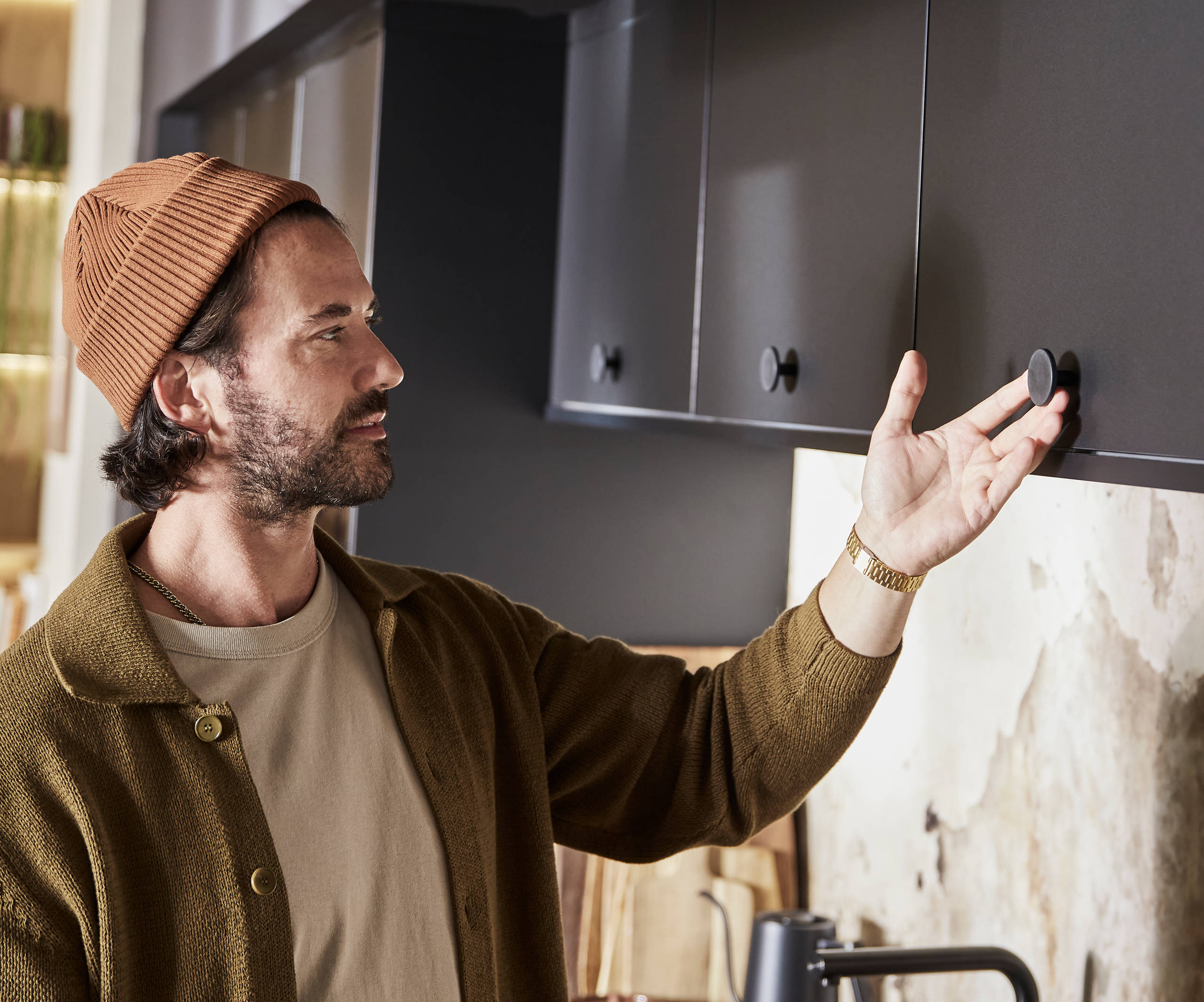Man wearing clothes in earth tones opening a top cabinet in Hoxton Sumi Black