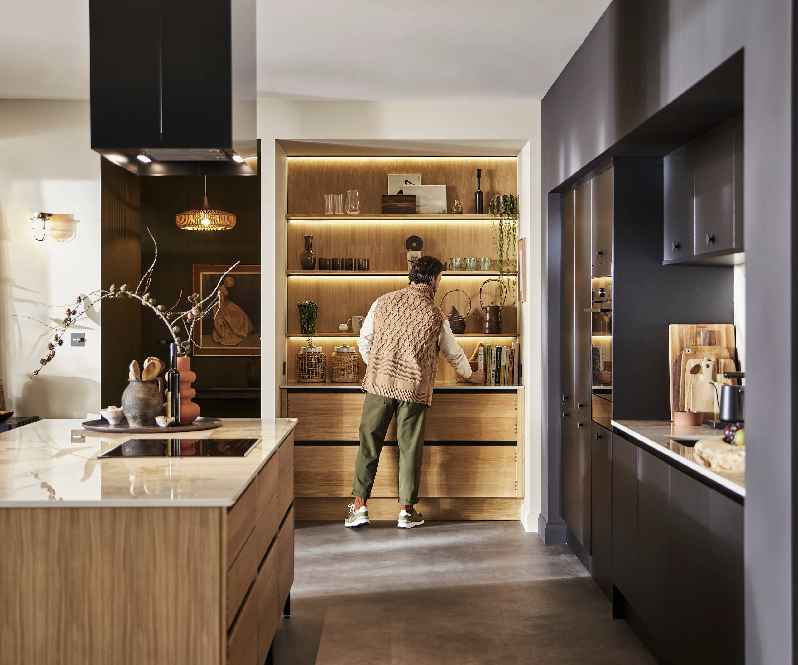 Man organising reaching for cook book in natural oak open shelves with matching wall paneling over Nordic Craft cabinetry.