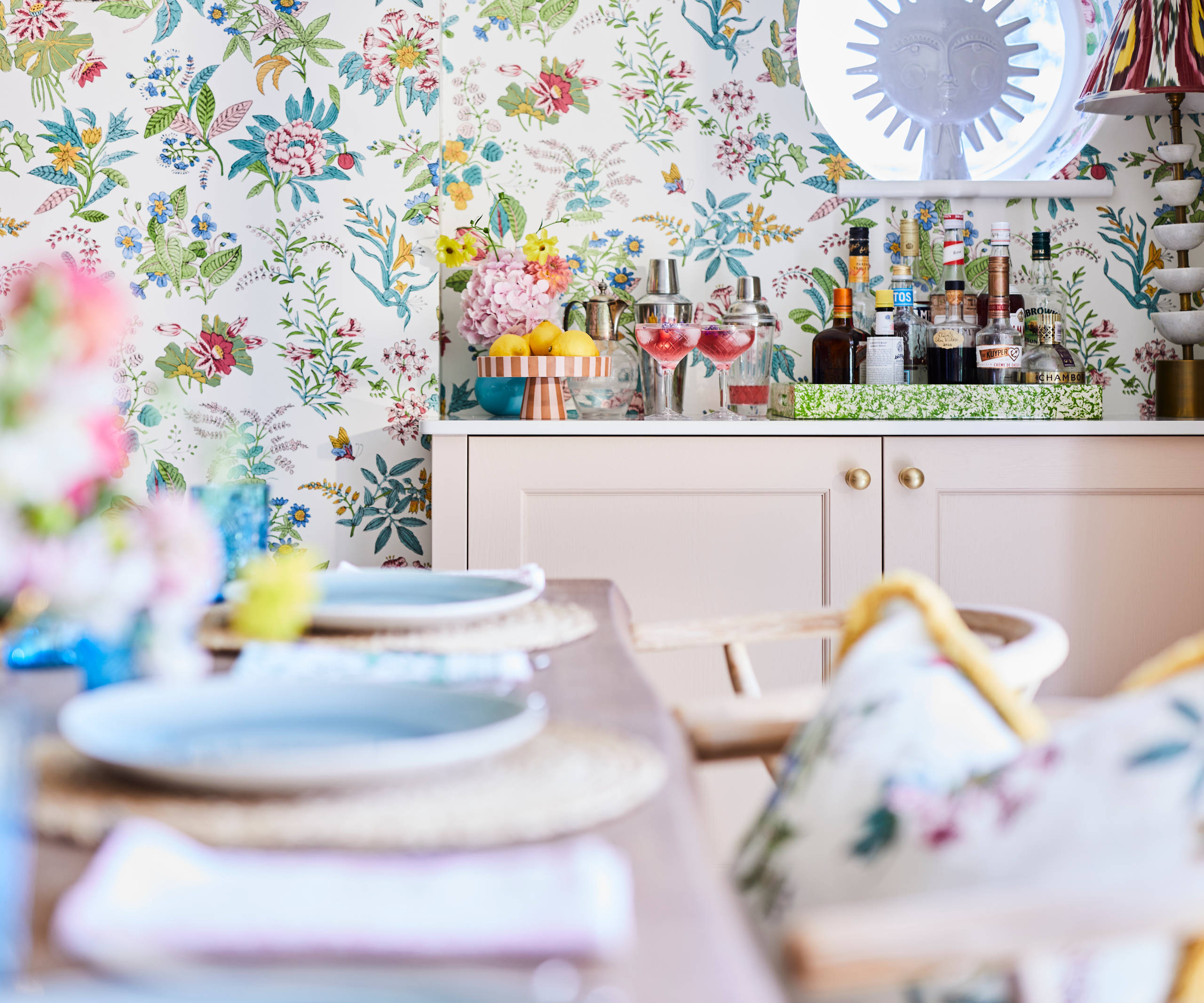 Cocktail corner in Sophie Robinsons maximalist Ludlow kitchen from Magnet, with a dining room table in foreground, floral pattern wallpaper.