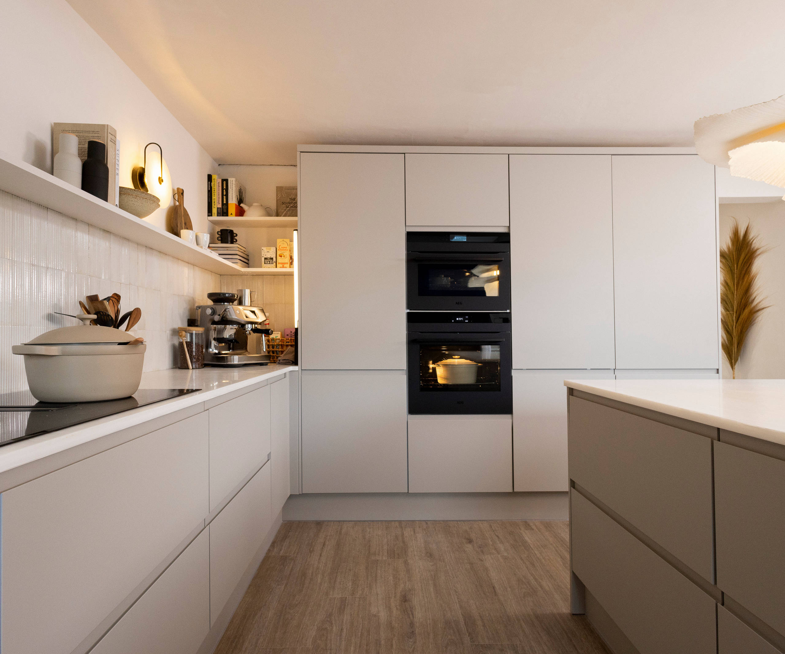 View of Yasmin Wyatt's open, light and airy neutral shade handleless Luna kitchen from Magnet, a white Corian worktop in Onyx, two AEG ovens integrated into tall cabinets.