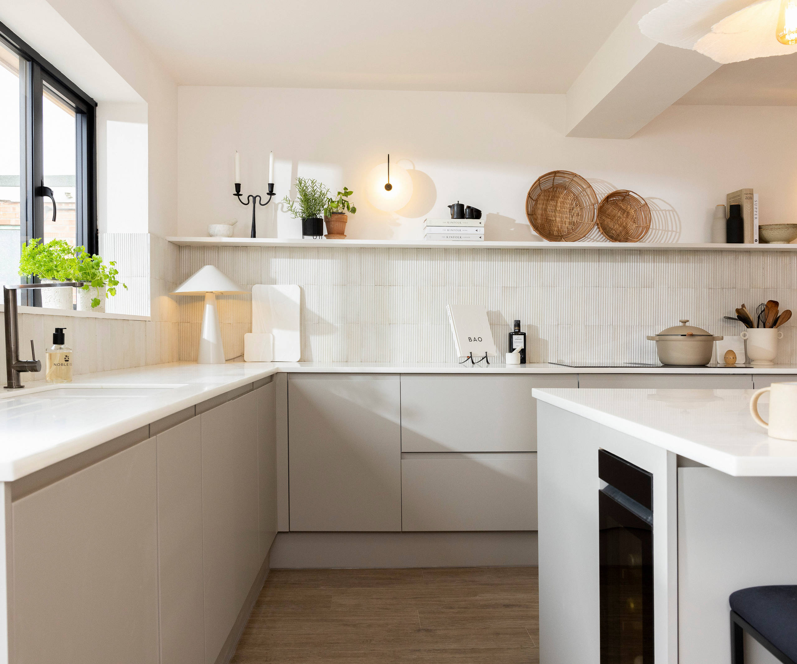 View of Yasmin Wyatt's open, light and airy neutral shade handleless Luna kitchen from Magnet, a white Corian worktop in Onyx, wine fridge integrated into kitchen island.