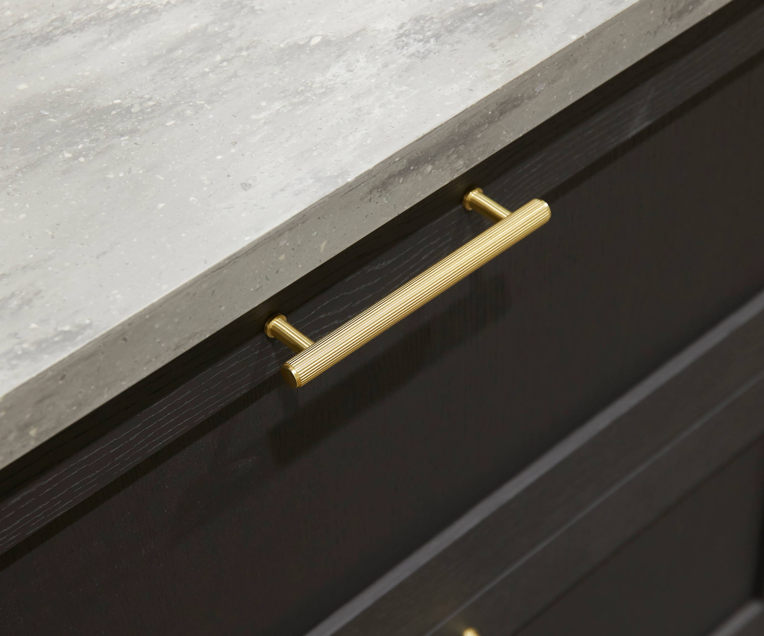 A close-up view of Ambleside drawer frontals in Graphite, with brass bar handles and grey worktop.