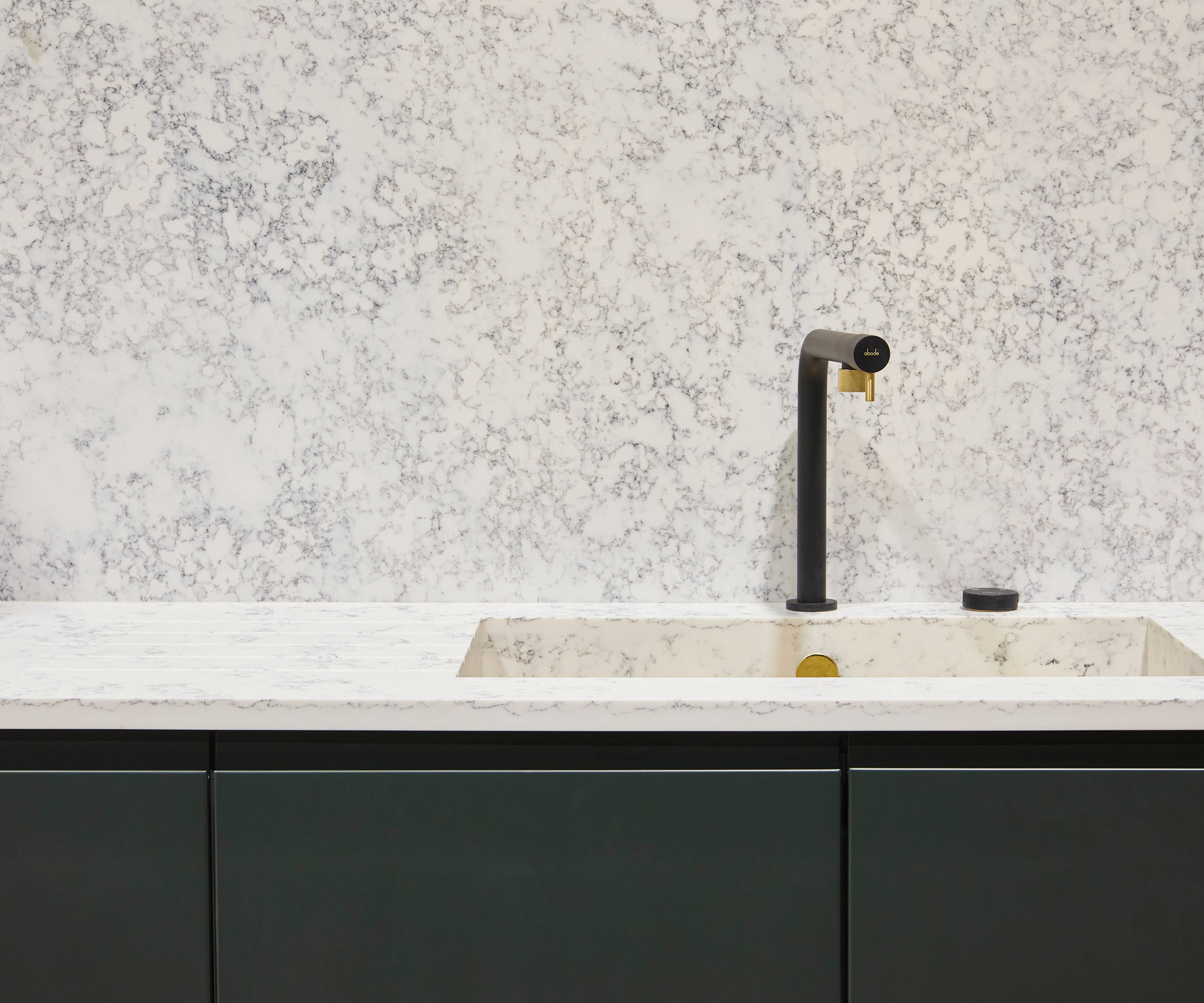 The Duxbury kitchen in rich green Arboretum, paired with white marble-effect worktops, built-in kitchen sink and a matte black and gold kitchen tap.