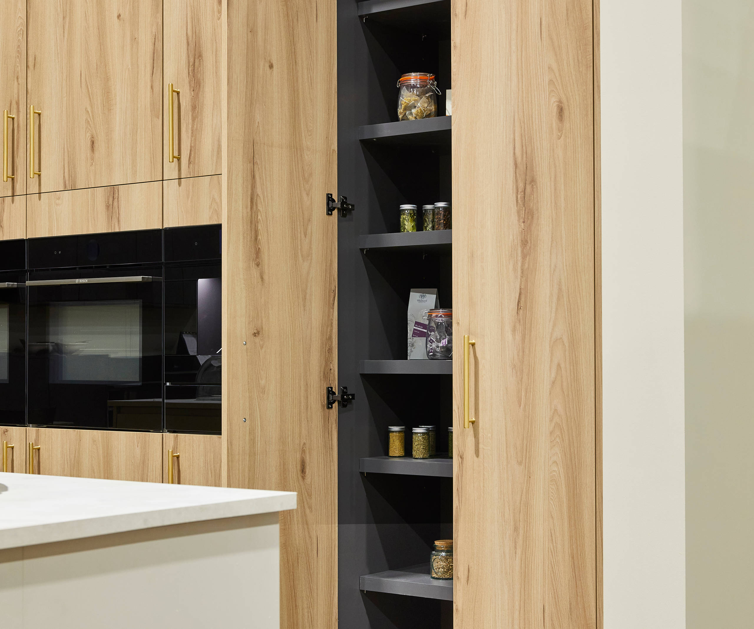 Magnet's modern Portobello kitchen in a light woodgrain décor, larders finished with brass bar handles.