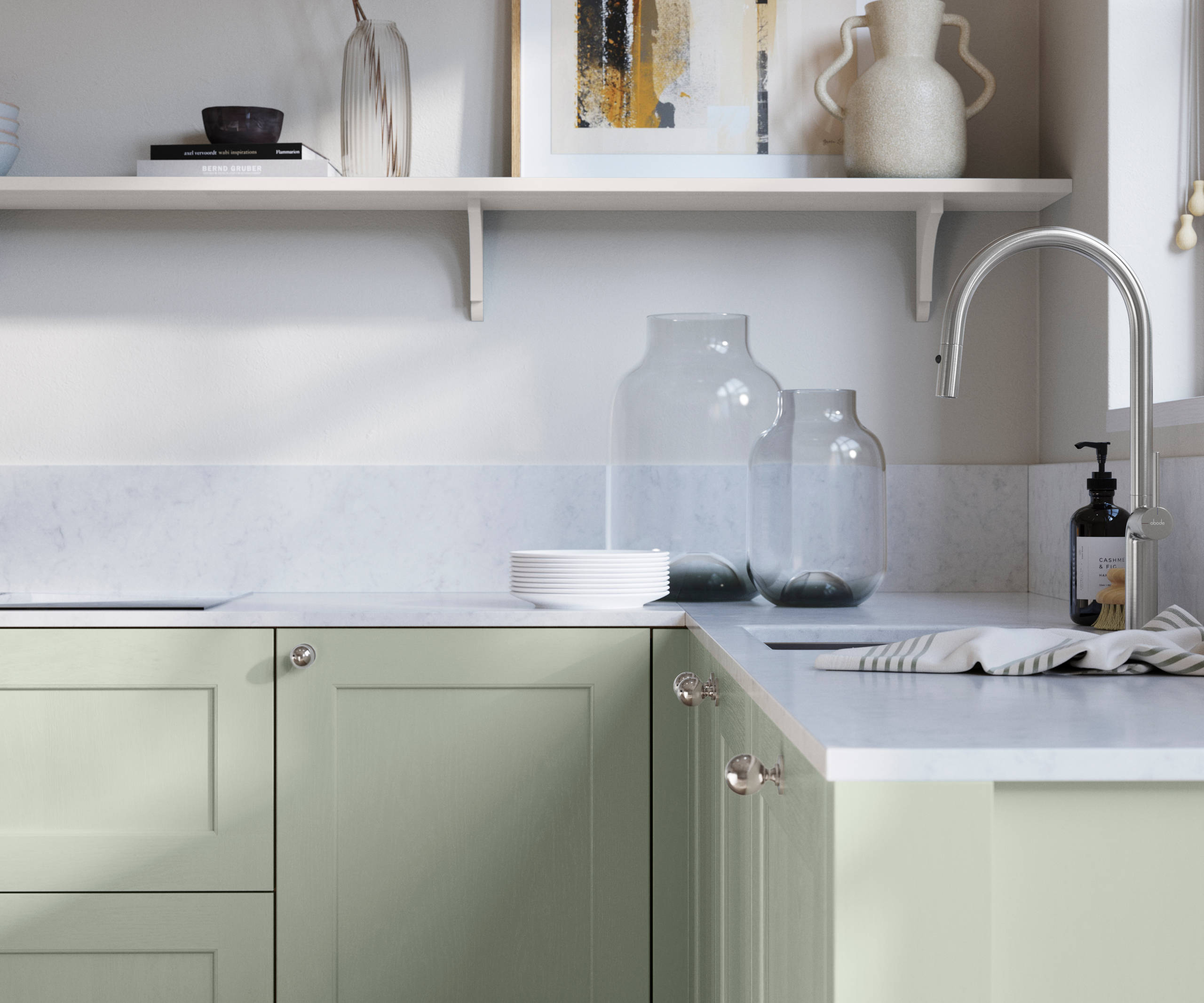 Ludlow, a traditional Shaker-style premium feel kitchen range with a visible woodgrain on its panelled doors here shown in the light shade Seagrass styled with steel knobs, steel tap, a white marbled worktop with matching splashback.